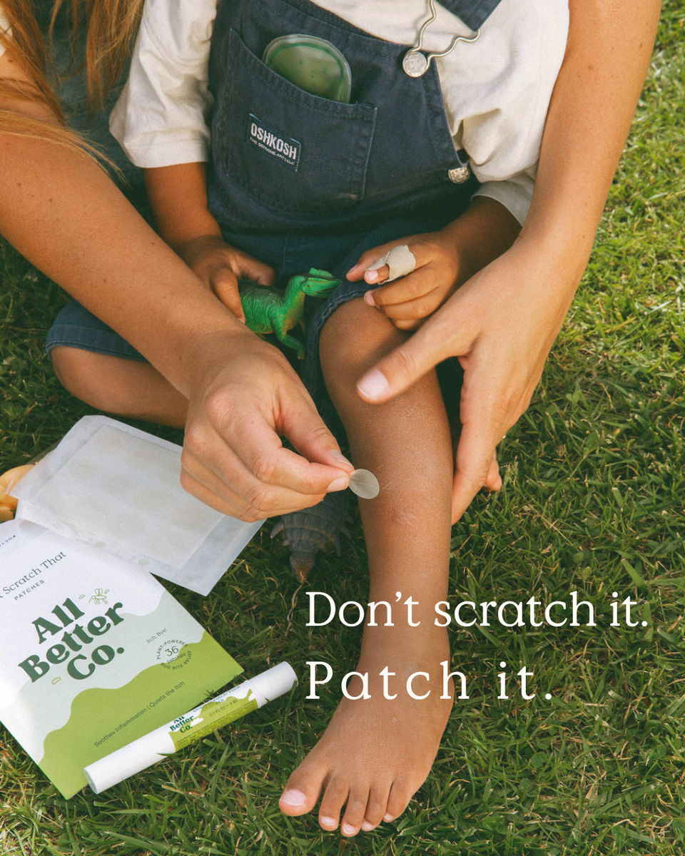 A child sitting on grass while an adult applies a silver bandage to the child's leg. A package labeled 'All Better Co.