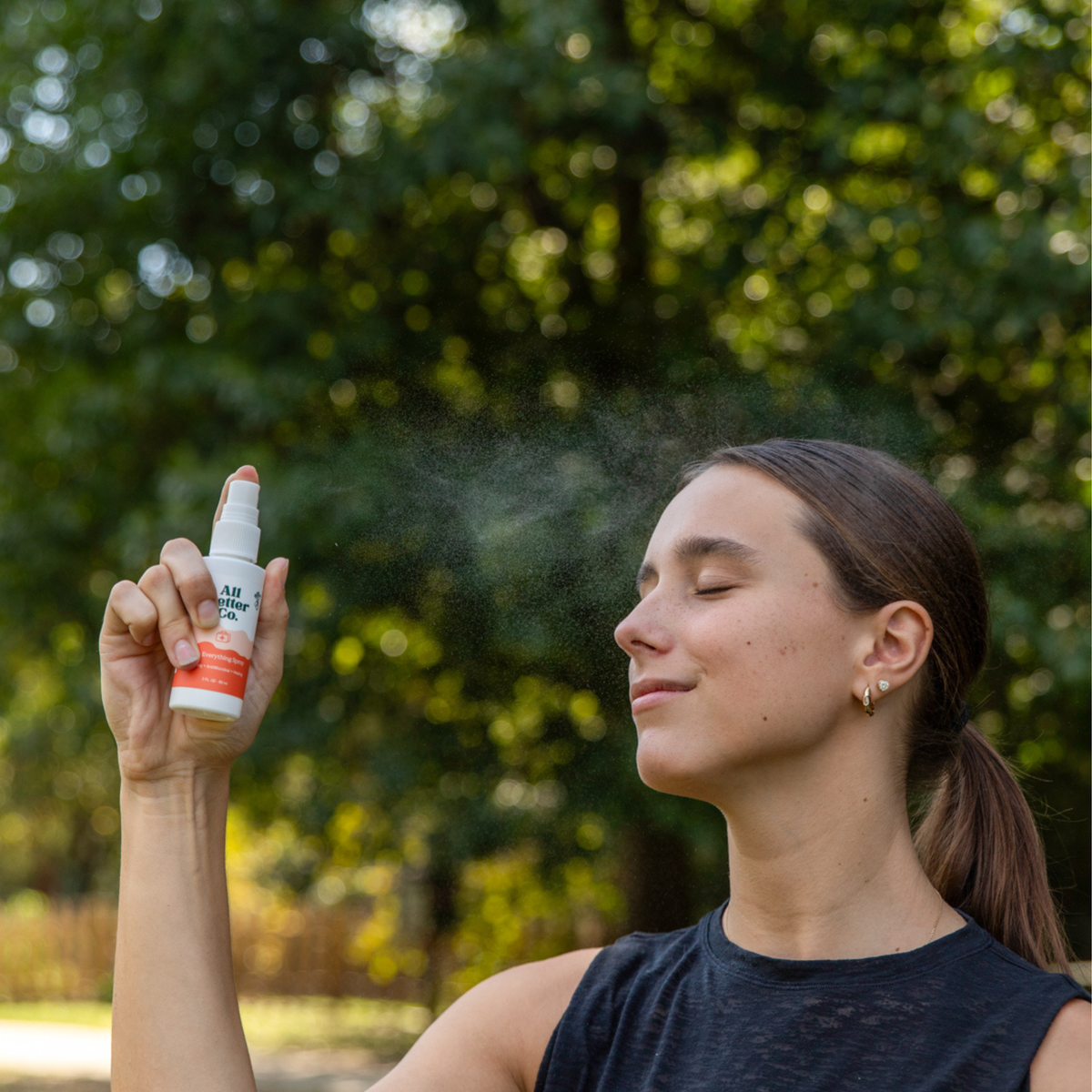 Woman applying a spray product outdoors with trees in the background