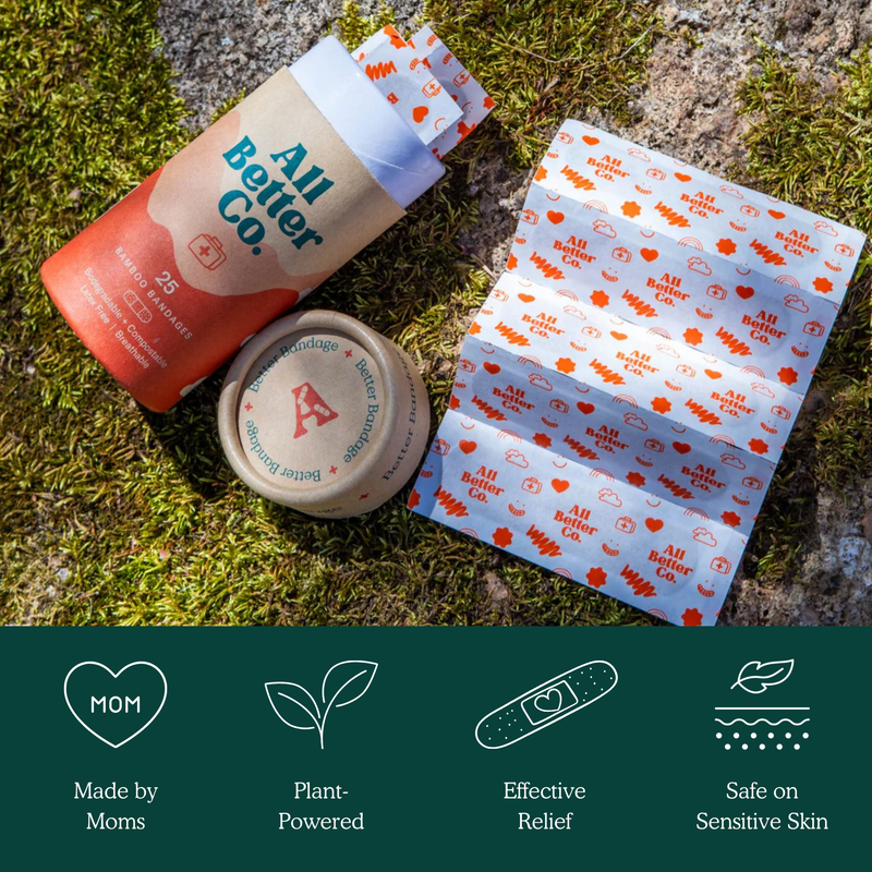 All Better Co. bandage kit shown outdoors on moss and rock, including a cylindrical container, a small round jar, and a folded box of bandages.
